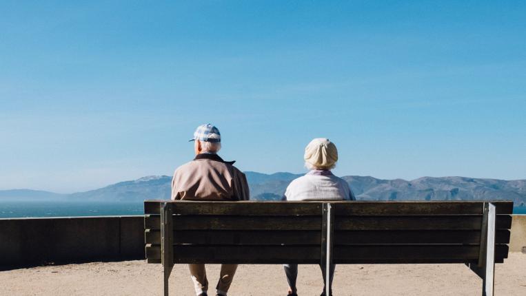 Dois idosos sentados num banco a olha para o infinito